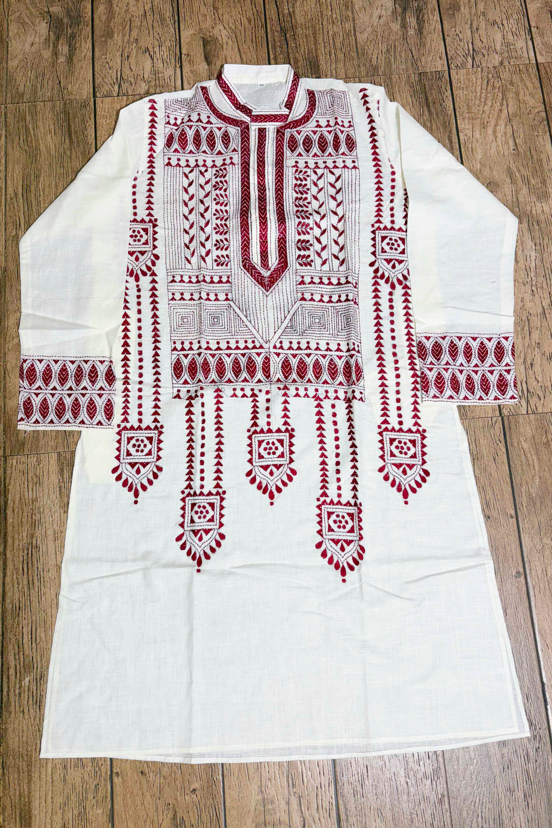 White embroidered kurta with red patterns on a wooden surface