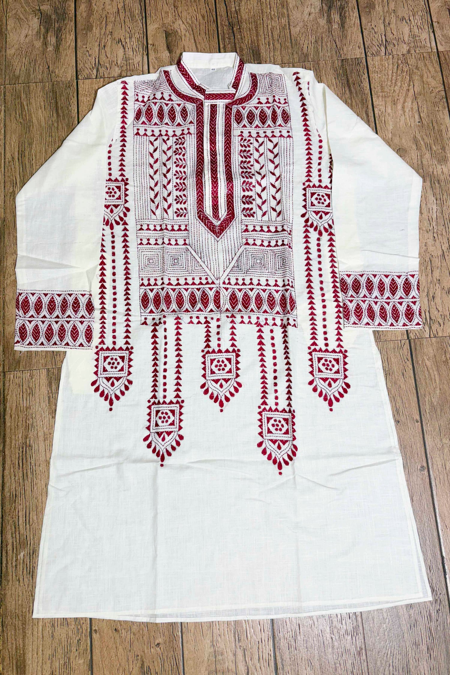 White embroidered kurta with red patterns on a wooden surface